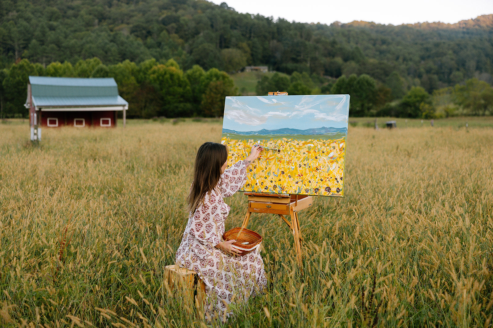 Woman painting a landscape with a barn and field in the background