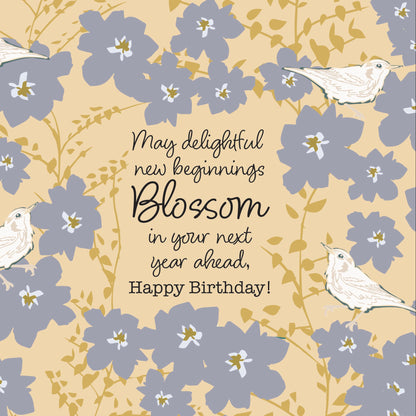 A floral birthday card design with the text 'May delightful new beginnings Blossom in your next year ahead. Happy Birthday!' centered among light blue blossoms, green stems, and four small white birds on a pale yellow background.